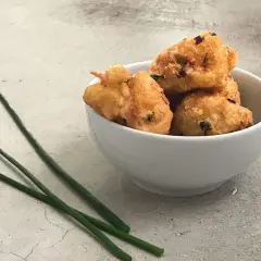 Tazón blanco con buñuelos de bacalao dorados y crujientes, decorado con cebollino fresco.