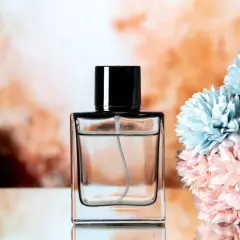 Elegancka butelka perfum z czarną nakrętką, obok bukiet pastelowych kwiatów. Chcesz wiedzieć, jak sprawdzić oryginalność perfum?
