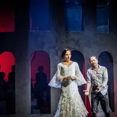 Carmen w białej sukni i mężczyzna na scenie operowej. Tło z łukami i czerwonymi światłami.