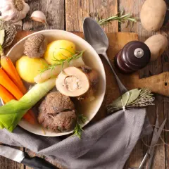 Un bol de pot-au-feu fumant avec des carottes, des pommes de terre, du poireau et de la viande. Des herbes et de l'ail complètent ce plat réconfortant.