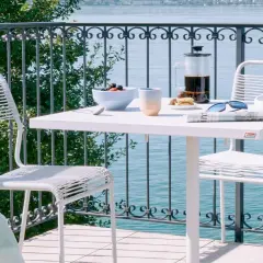 Idee per arredare balcone piccolo: tavolino bianco con caffè, frutta e sedie moderne, vista lago.