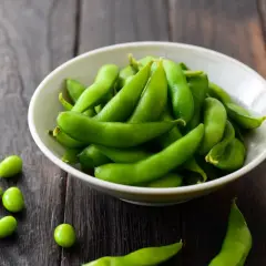 Miseczka pełna zielonej fasolki edamame na drewnianym tle. Kilka fasolek rozsypanych obok.