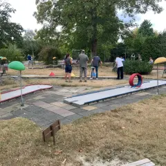 Familien spielen Minigolf Gummersbach. Bunte Bahnen mit Hindernissen wie einem roten Reifen laden zum Spiel ein.