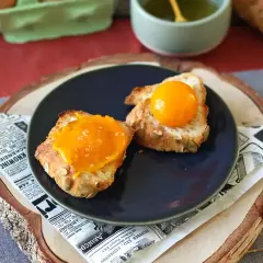 Sur une assiette, deux toasts de pain aux graines, l'un garni d'une texture orangée et l'autre d'un jaune d'œuf confit brillant.