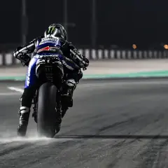 Piloto de MotoGP en plena acción, buscando el holeshot. La moto levanta polvo al acelerar en la noche.