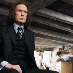 Bill Nighy jako Rufus Scrimgeour w Harry Potterze, w garniturze, siedzi w ponurym wnętrzu.