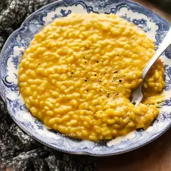 Un cremoso risotto zucca e rosmarino, servito su un piatto decorato, con una forchetta che affonda nella sua bontà.