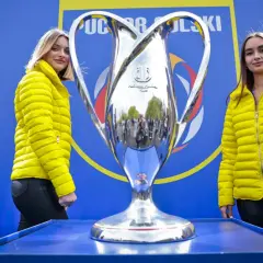 Dwie kobiety w żółtych kurtkach stoją obok lśniącego pucharu. Tło zdobi napis "Puchar Polski".