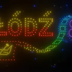 Niesamowite pokazy świetlne tworzą napis "ŁÓDŹ" i symbol rolki filmowej z kolorowych świateł na nocnym niebie.