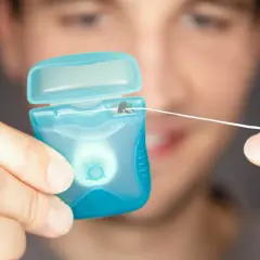 Mężczyzna trzyma niebieskie opakowanie z nicią dentystyczną (floss).