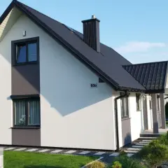 Nowoczesny dom z projektu Kamilek, z białym tynkiem i szarymi akcentami, otoczony zadbanym ogrodem.