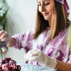 Frau wendet mit Handschuhen rote Farbe auf Stoff an, um Batik-Techniken zu erlernen.