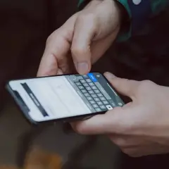 Dłonie trzymające smartfon z klawiaturą. Widoczna opcja "jak zwiększyć litery w telefonie" na ekranie.