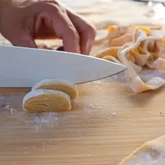 Eine Hand schneidet mit einem Messer frisch gerollte Teigrollen, um Makkaroni selber zu machen.