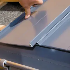 Dłoń układa metalowy panel dachowy, pokazując, jak zrobić rąbek stojący.