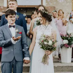 Para młoda trzymająca się za ręce, otoczona bańkami mydlanymi i gośćmi weselnymi.
