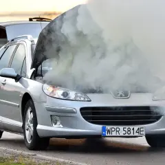 Srebrny Peugeot z otwartą maską i kłęby dymu wydobywające się z silnika. Rozbiegany silnik diesla dał o sobie znać.