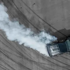 Czarny samochód driftuje, zostawiając za sobą gęsty biały dym na asfalcie.
