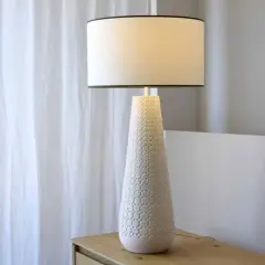 Elegante lámpara de mesa cerámica con base cónica texturizada y pantalla blanca, ideal para añadir un toque de estilo.