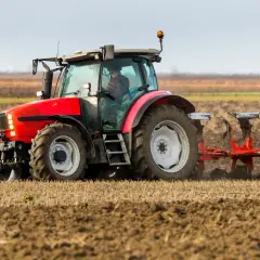 Czerwony traktor z pługiem orze pole. Rolnik przygotowuje ziemię, kiedy orka zimowa jest w pełni.