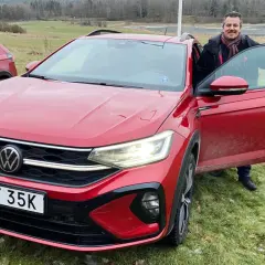 Man med halsduk vid en röd VW Taigo. Bilen är redo för ett vw taigo test i svensk natur.