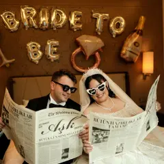 Para młoda czyta gazetę "The Wedding Post" z nagłówkami "Miłość", "Wielki dzień nadszedł!" i "Wszystkie przygotowania zakończone!". To ich przykładowy harmonogram wesela.