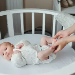 Delikatne nóżki noworodka w białej koronkowej kaftaniku, mama delikatnie je dotyka.