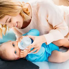 Uśmiechnięta mama karmi butelką dziecko. Ile powinno trwać karmienie butelką? To zależy od malucha.