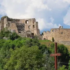 Ruiny zamku w Frysztaku, górujące nad zielonym wzgórzem, z drewnianym krzyżem na pierwszym planie.