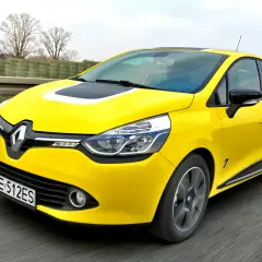 Żółty Renault Clio, jeden z popularnych francuskich marek samochodów, pędzi po drodze.