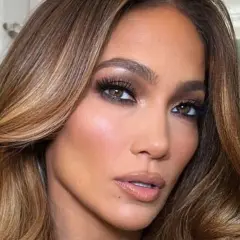 Primer plano de una mujer con maquillaje glamuroso y unos preciosos reflejos en pelo castaño que brillan con la luz.