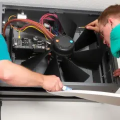 Técnicos revisan un aire acondicionado donde las aspas del aire acondicionado no se mueven. Cables y componentes expuestos.