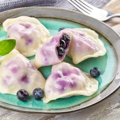 Pyszne pierogi z jagodami na turkusowym talerzu, ozdobione świeżymi borówkami i gałązką ziół.