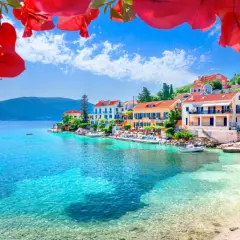 Kefalonia co zobaczyć: malownicza zatoka z turkusową wodą, kolorowe domki na wzgórzu i kwitnące bugenwille. Idealne miejsce na wakacje.