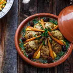 Ein Hähnchen-Tajine mit Karotten, Oliven und Zitrone, serviert in einem traditionellen Tontopf.