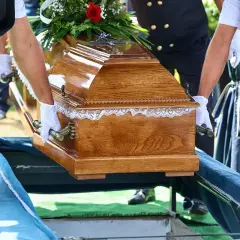 Tragarze w białych rękawiczkach niosą drewnianą trumnę. Nawet bez ubezpieczenia, zasiłek pogrzebowy na nieubezpieczonego członka rodziny jest możliwy.