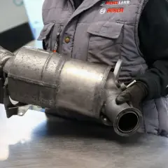 Mechanik w rękawiczkach trzyma element układu wydechowego. To część do diesla bez DPF, gotowa do montażu lub wymiany.