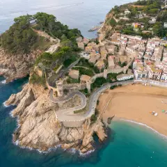 Widok z lotu ptaka na Tossa de Mar z kamiennymi murami obronnymi, wieżami i plażą.