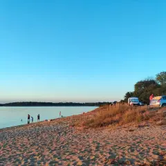 Piękny dzień nad jeziorem Dzierżno Duże. Ludzie kąpią się, a obok zaparkowane samochody i kampery.