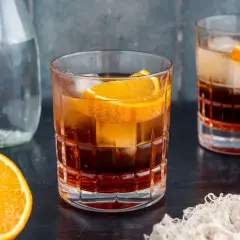 Ein erfrischender Americano Cocktail mit Eis und Orangenscheiben, daneben eine Karaffe Wasser und frische Orangen.
