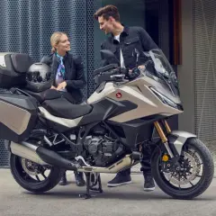 Pareja sonriente junto a una Honda NT 1100, lista para viajar. Opiniones positivas sobre su comodidad y diseño.