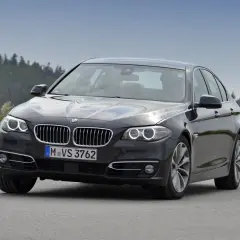 Ciemnoszary sedan BMW F10 na drodze, z widokiem na las. Idealne wymiary dla komfortowej podróży.