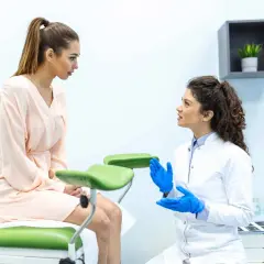 Lekarka w niebieskich rękawiczkach wyjaśnia pacjentce, jak prawidłowo używać tampon w cipce.