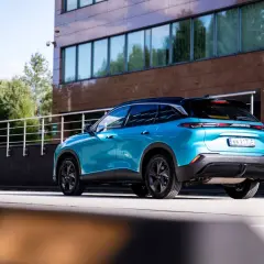 Błękitny BAIC 5 z czarnym dachem stoi przed nowoczesnym budynkiem.