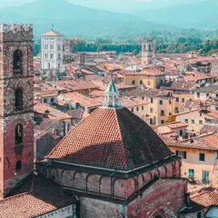 View over a walled city in Tuscany, with terracotta roofs, ancient towers, and distant mountains.