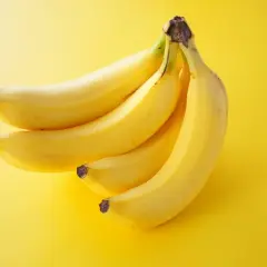 Pęczek żółtych bananów na żółtym tle. Zastanawiasz się, ile kalorii ma średni banan?