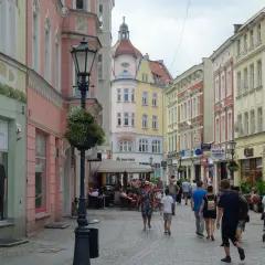 Kolorowa ulica z kamienicami, latarnią i ludźmi spacerującymi po deptaku. Zielona Góra oferuje wiele atrakcji.