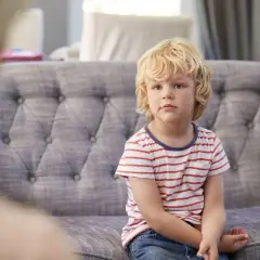Chłopiec z blond włosami siedzi na kanapie w paski.