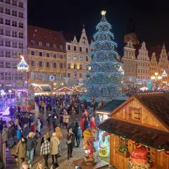 Tłoczny jarmark we Wrocławiu nocą. Rozświetlona choinka, kramy i tłumy ludzi tworzą magiczną atmosferę.