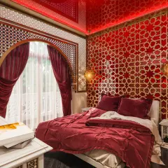 Luksusowa sypialnia w stylu marokańskim. Czerwone ściany z geometrycznymi wzorami, bogato zdobione łóżko i orientalne lampy tworzą magiczną atmosferę.